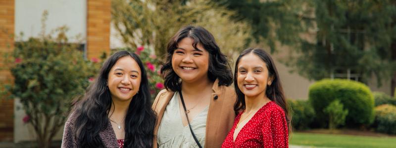 Three international female students standing on the Langley campus smiling at the camera.